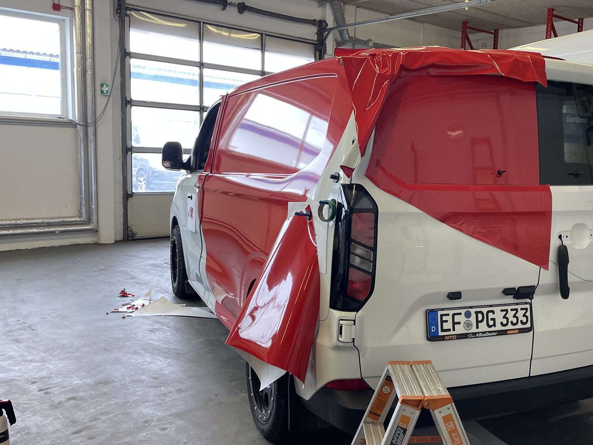 Transporter in der Halle, rote Folie wird auf Seitenwand und Heck aufgezogen