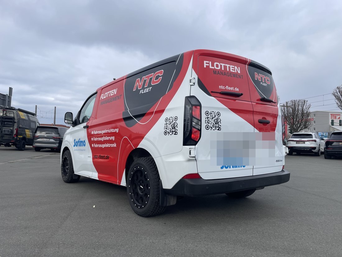 Beklebter Transporter von NTC Fleet in den Hausfarben Rot und Weiß, Heckansicht vor der Werkstatt